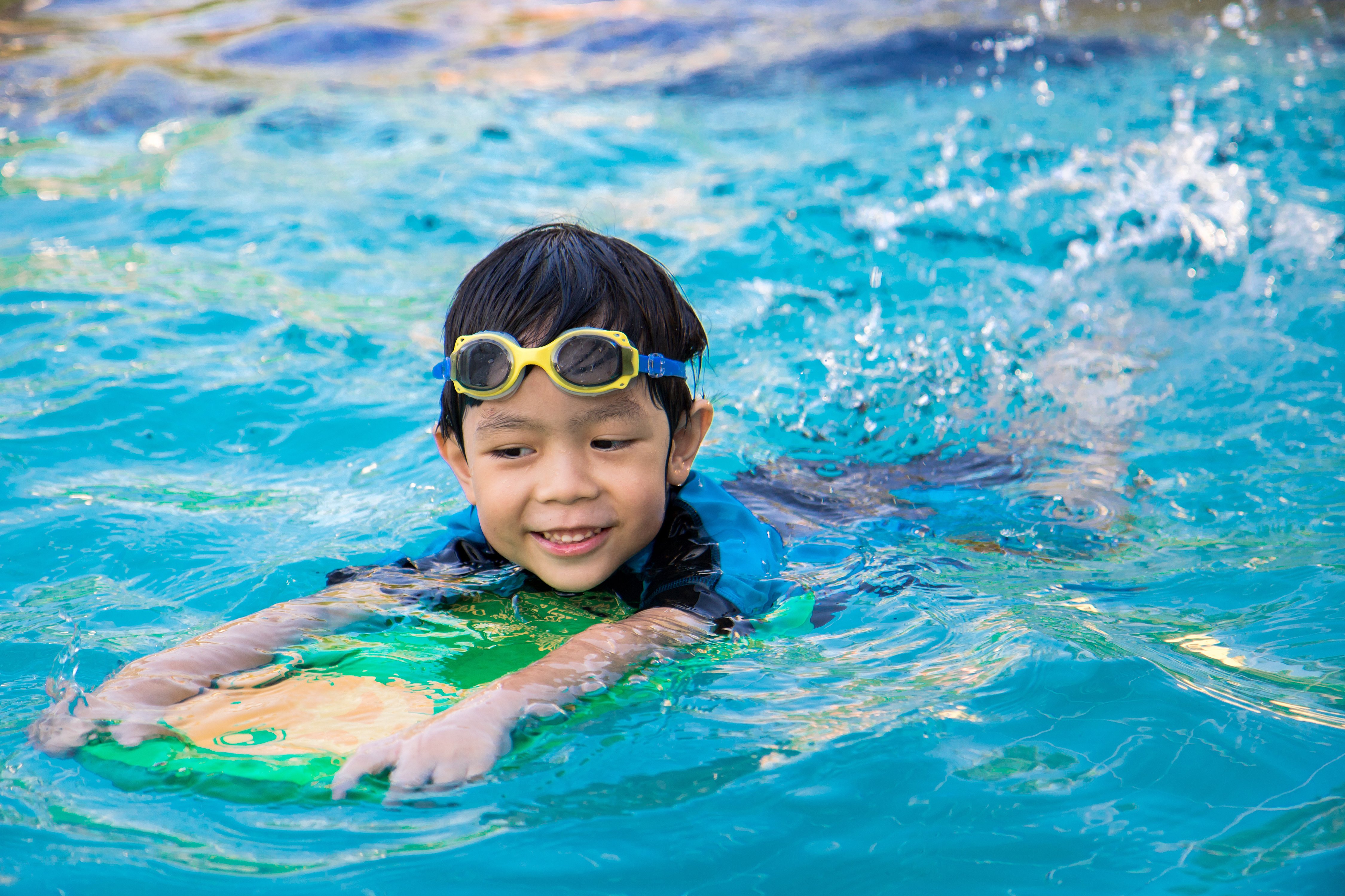 Young boy in pool with floating board learning to swim