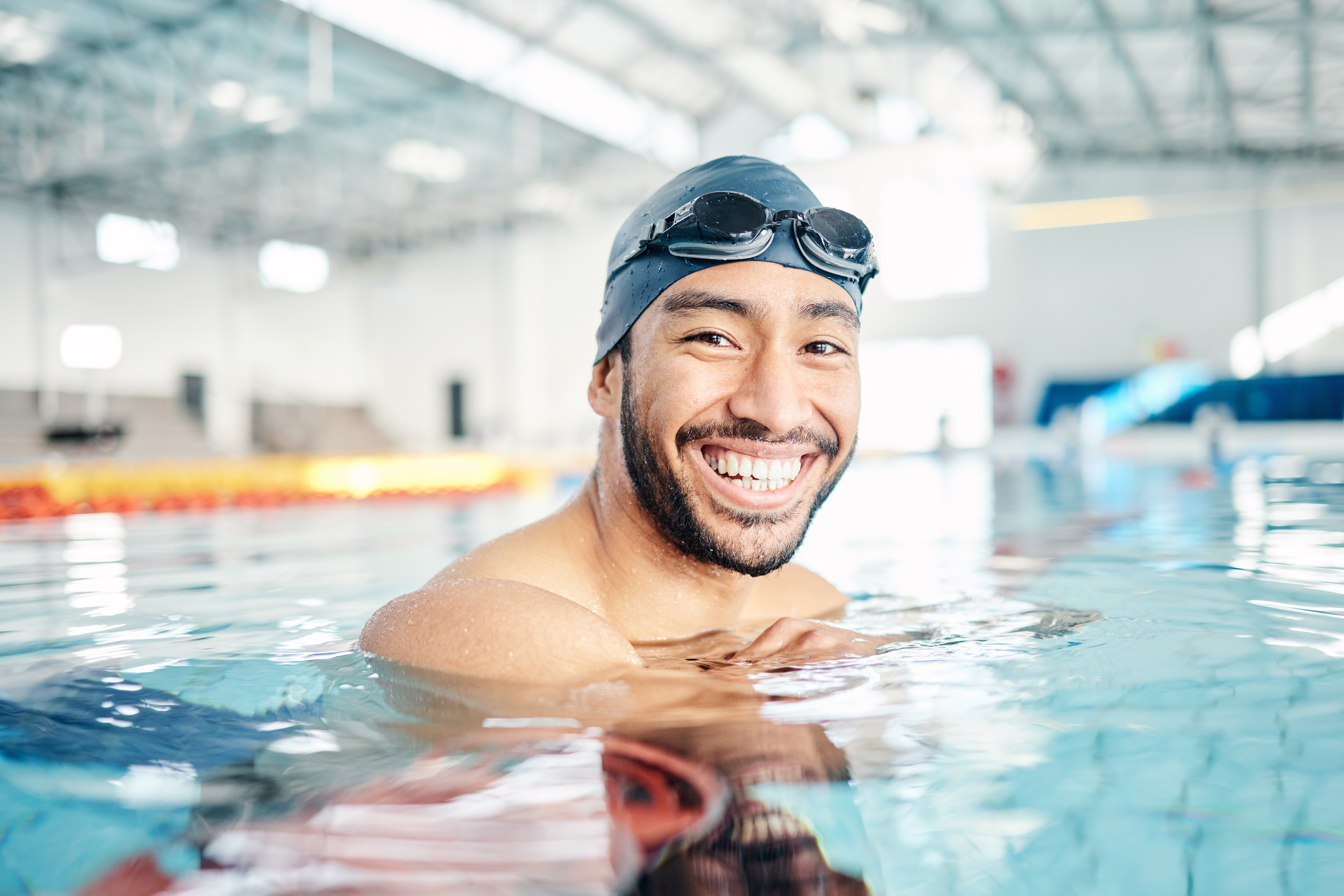 Man with swim cap and goggles smiling in pool