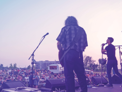 A band on stage looking out at the crowd on a summer day